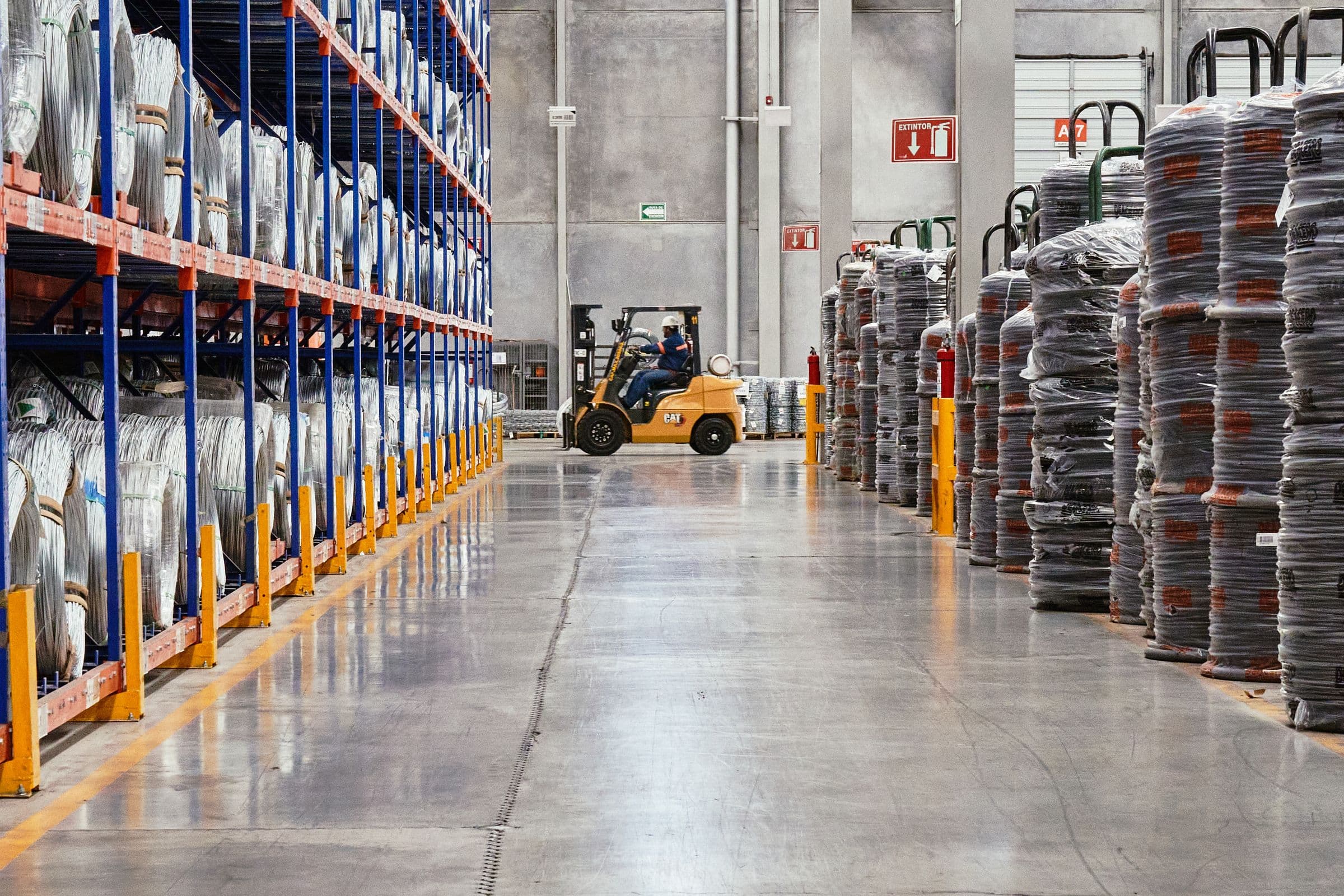 A forklift working down an aisle of a large, well stocked warehouse